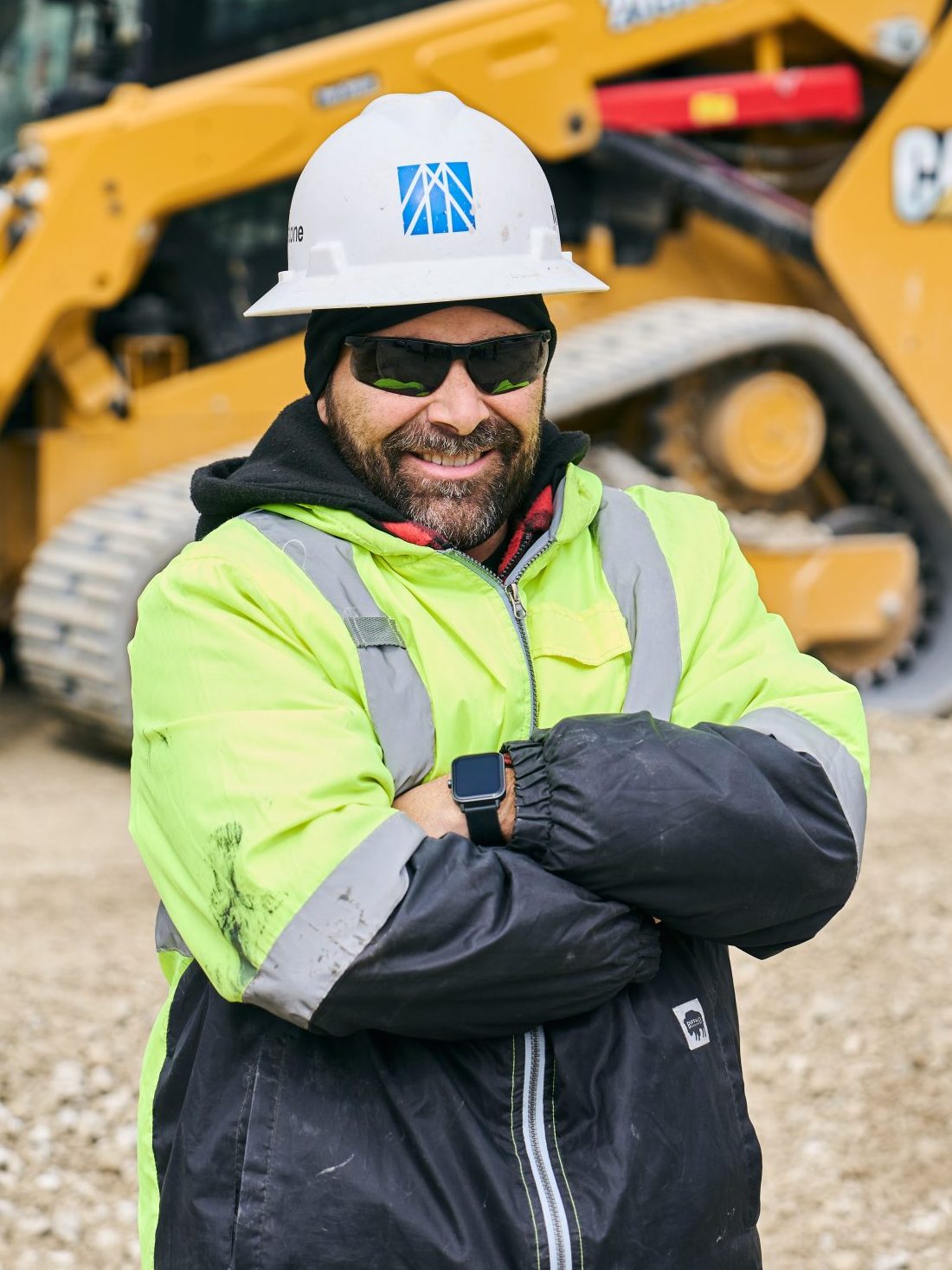 hispanic construction worker standing in front of a skid steer.