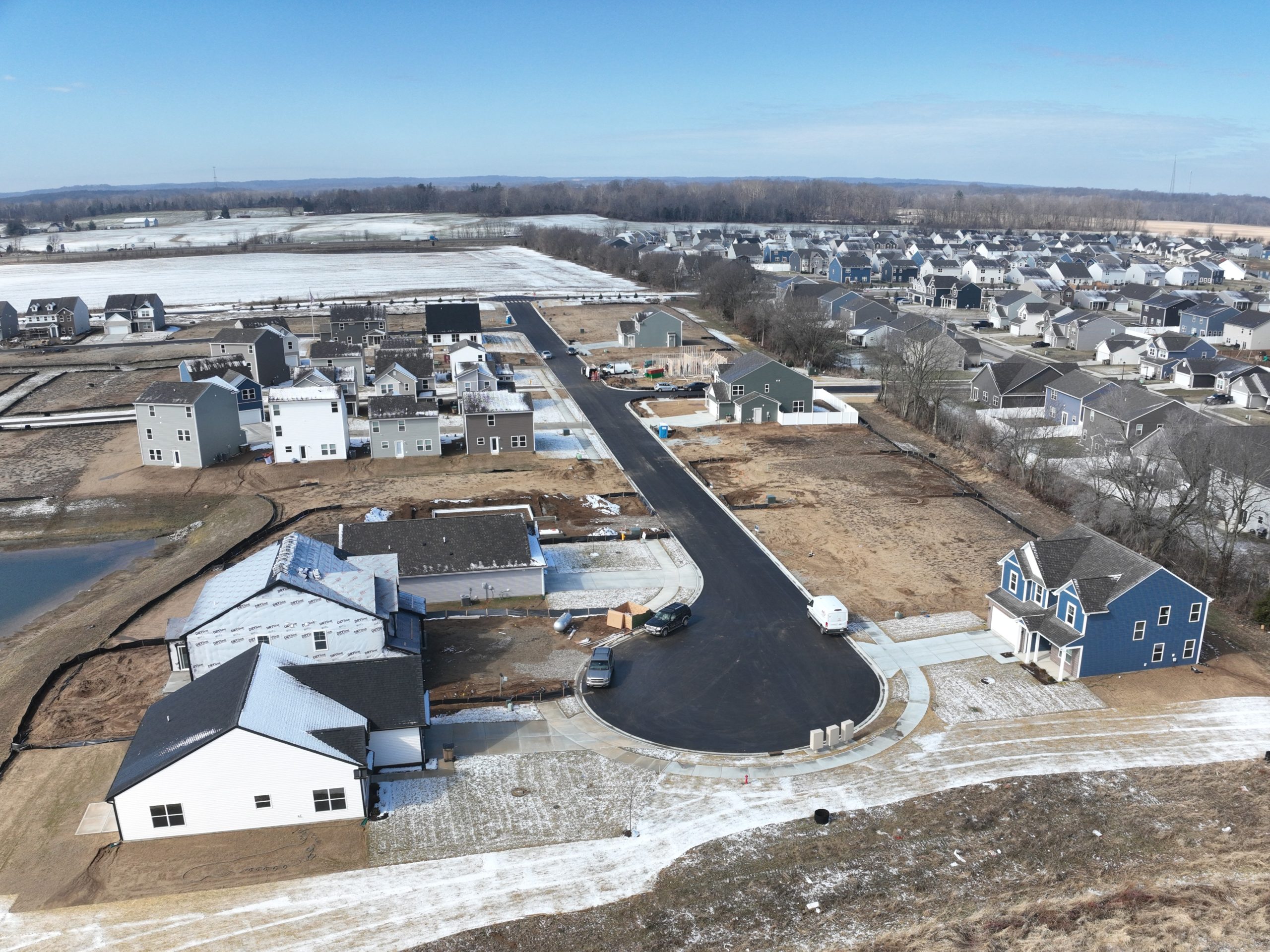 A partially built neighborhood is viewed from above. The shot includes asphalt roads leading to new houses and nearby waiting plots of land.